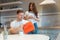 Young happy woman greeting her surprised husband with present in red bag on saint valentine`s day during breakfast in the kitchen