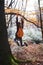 Young happy woman hanging on tree in woods with orange backpack. Funny girl fooling around on a forest background.
