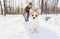Young happy woman having fun in snowy winter park with Corgi baby dog
