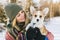 Young happy woman having fun in snowy winter park with Corgi baby dog