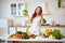 Young happy woman holding broccoli and cabbage in the beautiful kitchen with green fresh ingredients indoors. Healthy food and