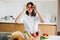 Young happy woman holding cherry tomato at eyes and showing kiss on background of modern white kitchen. Healthy food concept. Home