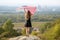 Young happy woman with long hair raising up waving on wind american national flag in her hands standing on high rocky hill