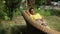 Young happy woman lying on wicker sofa with flowers blooming at background. Portrait of relaxed attractive African