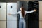 Young happy woman in mask leaning on her new refrigerator in a mall
