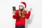 Young happy woman in a red Santa Claus hat and a medical mask on her face, waving, making a video call on a smartphone on