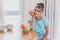 Young Happy Woman Refreshing with Cup of Coffee, Snacks and Fresh Fruit at the Kitchen Table in the Early Morning.