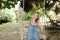 Young happy woman riding swing and making selfie by smartphone, sand and trees in background.