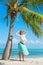 Young happy woman standing on beach under palm tree