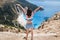 Young happy woman standing on top of a rock, raising hands with an exciting feeling of freedom, looking at Myrtos Beach