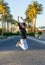 Young happy woman in sunglasses is jumping in front of the palm trees at sunset