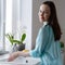 Young happy woman washing dishes in sink in front of window, soft early morning light