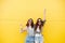 Young happy women friends standing over yellow wall