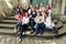 Young happy women sitting on stairs posing on background of old european city street, stylish hipster girls, moments of happiness