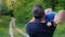 A young healthy father walks with his son in the park. Carries a baby in his arms, rear view