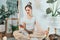 Young healthy woman using phone for setting mobile app for meditation at home, sitting in lotus position on floor