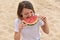 Young healthy woman in white t-shirt eat watermelon slice in summer on beach on sand background