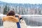 Young hiker girl with in down jacket making photos of river and forest in winter. Travel concept