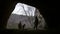 Young hiker in helmet enters to the dark cave with flashlight and deep forest at background