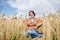 Young hippie woman with red burgundy hair, wearing boho style clothes, sitting in middle of wheat field, meditating, thinking,