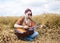 Young hippie women with red hair, wearing boho style clothes, sitting in the middle of wheat field, playing guitar. Travel