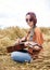 Young hippie women with red hair, wearing boho style clothes, sitting in the middle of wheat field, playing guitar. Travel