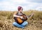 Young hippie women with red hair, wearing boho style clothes, sitting in the middle of wheat field, playing guitar. Travel