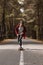 A young hipster in a cap and plaid shirt is riding his longboard on a country road in the forest