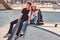 Young hipster couple trendy dressed relaxing together with skateboards on a skatepark on a sunny day.