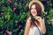 Young hipster girl wearing hat walking by blooming roses. Woman enjoys flowers in park. Summer outfit