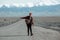 Young hipster hitchhiking on lonesome road with mountains in background