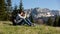 Young hipster man with backpack stands on top of mountain, enjoying amazing view. Male tourist takes a photo in the