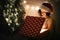 Young hipster woman in santa hat opening magical present in dark room at modern christmas tree. Merry Christmas. Stylish happy