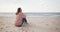 Young hipster woman sitting on a beach looking far away hugging knees