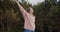 Young hipster woman standing in a forest rising hands high up feeling freedom