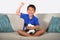 Young hispanic boy happy and excited watching football game on television at home living room couch celebrating scoring goal gestu