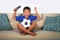 Young hispanic boy happy and excited watching football game on television at home living room couch celebrating scoring goal gestu