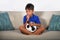 Young hispanic boy happy and excited watching football game on television at home living room couch celebrating scoring goal kissi