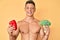 Young hispanic boy shirtless holding broccoli and red pepper winking looking at the camera with sexy expression, cheerful and