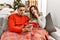 Young hispanic couple sitting on the sofa on christmas serious face thinking about question with hand on chin, thoughtful about