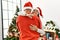 Young hispanic couple smiling happy and hugging holding engagement ring standing by christmas tree at home