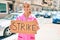 Young hispanic doctor woman smiling happy holding strike banner cardboard at street of city