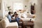 Young Hispanic family sitting on sofa reading a book together in the living room, seen from doorway