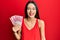 Young hispanic girl holding 100000 indonesian rupiah looking positive and happy standing and smiling with a confident smile