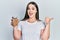 Young hispanic girl holding lentils bowl pointing thumb up to the side smiling happy with open mouth