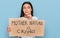 Young hispanic girl holding mother nature is crying protest cardboard banner serious face thinking about question with hand on