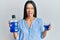 Young hispanic girl holding mouthwash for fresh breath sticking tongue out happy with funny expression