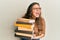 Young hispanic girl holding a pile of books angry and mad screaming frustrated and furious, shouting with anger