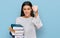 Young hispanic girl holding a pile of books annoyed and frustrated shouting with anger, yelling crazy with anger and hand raised