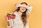 Young hispanic girl holding strawberries smiling cheerful playing peek a boo with hands showing face